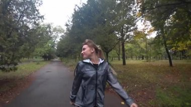 Yağmurlu bir sonbahar gününde parkta yürüyüş uzun saçlı güzel genç sarışın kız... Ağır çekim.