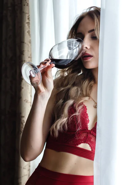 Чувственная молодая женщина в красном белье пьет вино nea окно . — стоковое фото