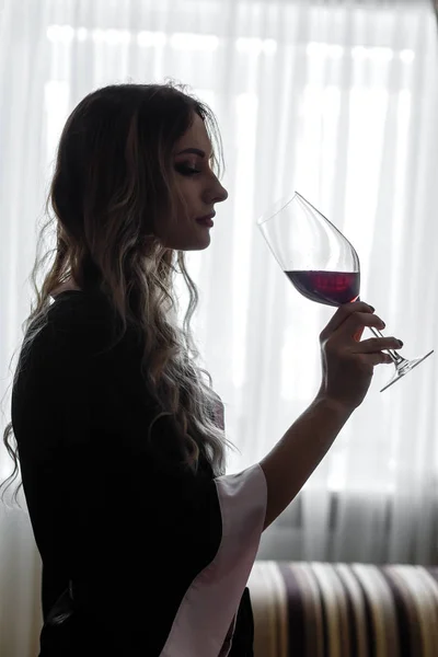 Sensual jovem mulher vestida com um roupão bebe um vinho de vinho — Fotografia de Stock