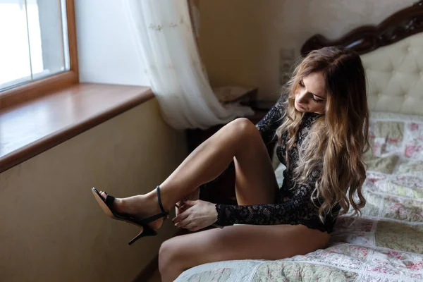 Bela jovem mulher vestida de lingerie preta senta-se em uma cama , — Fotografia de Stock