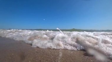 Dalgalar deniz güneşli yaz gününde güzel bir kumsalı bir kamera kapağı. Düşük bir açıdan, ağır çekim kamera için çekim.