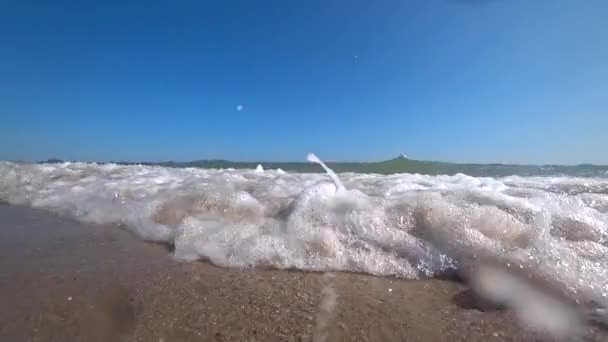 Les vagues de la mer couvrent une caméra sur une belle plage de sable par une journée d'été ensoleillée. Prise de vue pour caméra d'action à angle bas, au ralenti . — Video