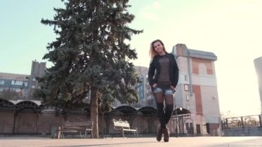 Uzun sarı saçlı, genç ve güzel bir kız. Gün doğumunda kaldırımda yürürken dinleniyor.,