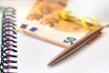 Lüks Kalem, Koruyucu Maske ve 50 Euro 'luk banknotlar beyaz kağıt defter üzerine. Avrupa 'da ekonomik kriz ve koronavirüs pandemisi. Alanın Sığ Derinliği, Seçici Odaklanma.