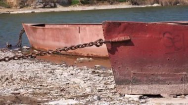 Güneşli bir günde nehir kıyısında zincirlenmiş iki eski paslı metal tekne.