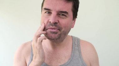 Yakışıklı, orta yaşlı, sakallı bir adam kameraya bakarak cilt kremi sürüyor. Sağlıklı cilt bakımı, erkek güzellik konsepti.