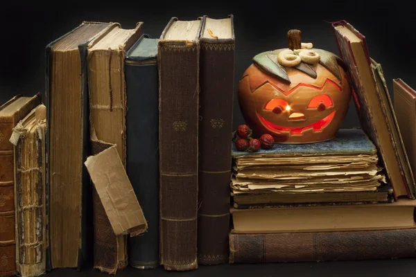Pumpkin lantern for Halloween and the old witch books. Head carved from a pumpkin on Halloween. Pumpkin tradition. The book of spells, magical book. Textbooks for witches.