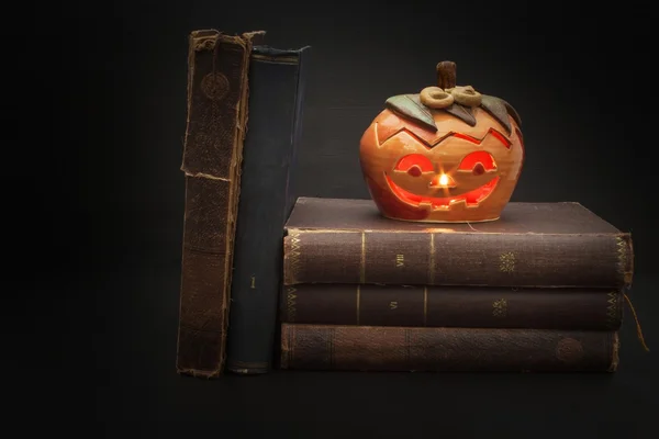 Pumpkin lantern for Halloween and the old witch books. Head carved from a pumpkin on Halloween. Pumpkin tradition. The book of spells, magical book. Textbooks for witches.