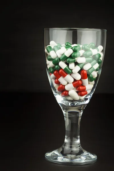 Verre de pilules vitamines. Drogues dans un récipient en verre sur fond noir. Compléments nutritionnels pour sportifs. Concept de régime alimentaire . — Photo