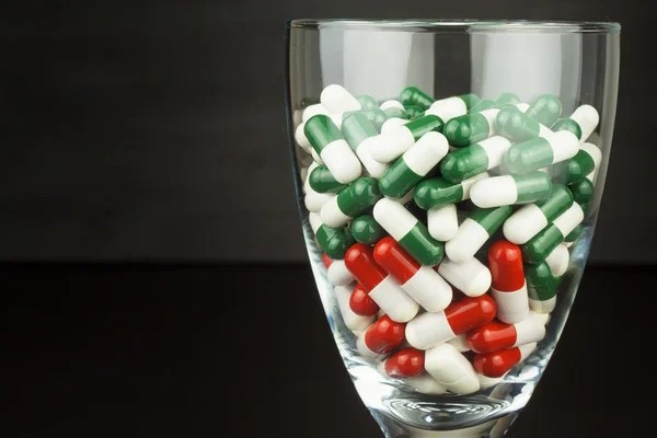 Un vaso de pastillas vitaminas. Drogas en un recipiente de vidrio sobre un fondo negro. Complementos nutricionales para deportistas. Concepto de dieta . —  Fotos de Stock