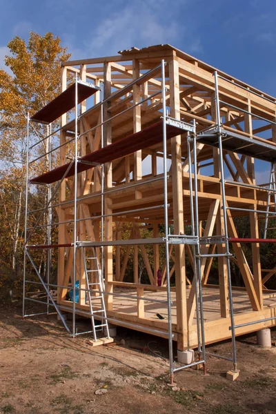 Andamios metálicos alrededor de la casa sin terminar. Construcción de casa ecológica. Marco de madera de la casa en construcción.Construcción nueva enmarcada de una casa. Casa de madera en proceso de construcción — Foto de Stock