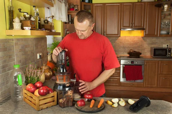 Hombre haciendo en la cocina jugo de manzana con zanahoria. Producción de bebidas de frutas. Frutas y hortalizas transformadas . —  Fotos de Stock