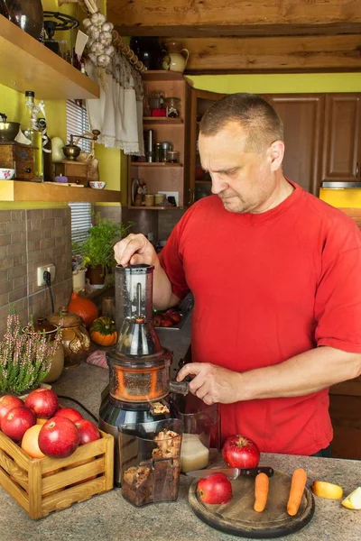 Hombre haciendo en la cocina jugo de manzana con zanahoria. Producción de bebidas de frutas. Frutas y hortalizas transformadas . —  Fotos de Stock
