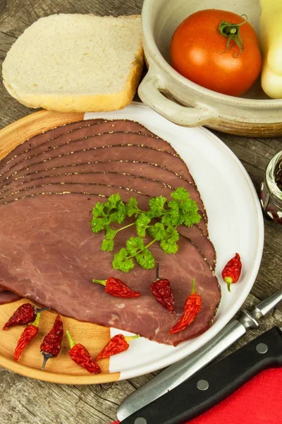 Rôti de bœuf froid sur une table en bois. Délicatesse du bœuf. Préparation de rafraîchissements froids. Repas traditionnel. Rôti de boeuf au poivre vert et piments et légumes . — Photo