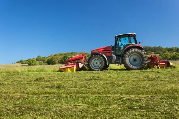 Pekerjaan pertanian. Traktor merah memotong padang rumput, Republik Ceko. Petani memanen jerami . — Stok Foto