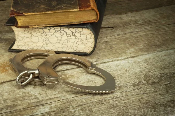 Βιβλίο και χειροπέδες σε ένα ξύλινο τραπέζι. Η έννοια της τιμωρίας και της δικαιοσύνης. Ποινή για ένα έγκλημα. Διαφθοράς και τιμωρίας. Σύλληψη εγκληματιών. — Φωτογραφία Αρχείου