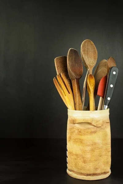 Εργαλεία μάγειρας σε ένα ξύλινο ράφι. Σκεύη κουζίνας σε ένα κεραμικό δοχείο σε μαύρο φόντο. — Φωτογραφία Αρχείου