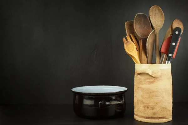 Narzędzia gotować na drewnianą półkę. Naczynia kuchenne w ceramicznym pojemniku na czarnym tle. — Zdjęcie stockowe