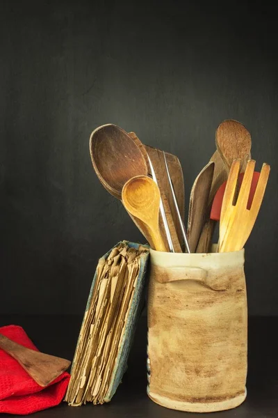 Outils cuire sur une étagère en bois. Ustensiles de cuisine dans un récipient en céramique sur fond noir . — Photo