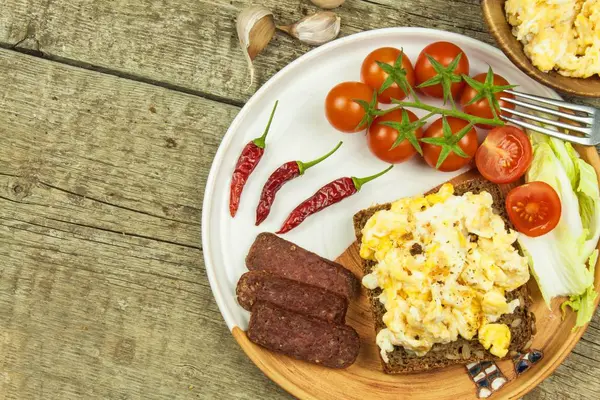 Scrambled eggs with bread and salami. Egg breakfast on a wooden table. Healthy food. — Stock Photo, Image