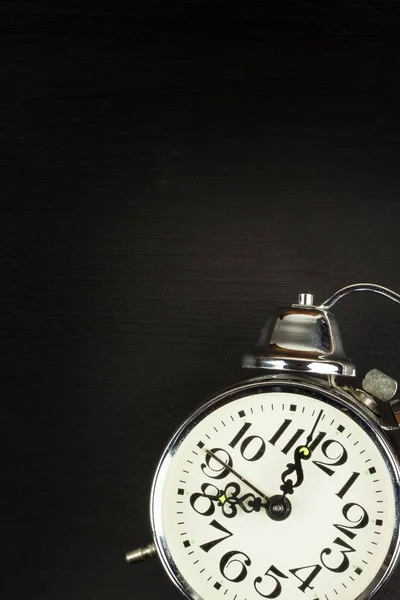 Retro metal alarm clock on a black wooden background. Open your eyes. Reveille to wake up. Place for text.