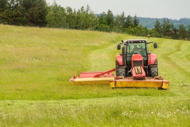 Bir tarım çiftliğinde çalışmak. Kırmızı bir traktör çayırı keser.