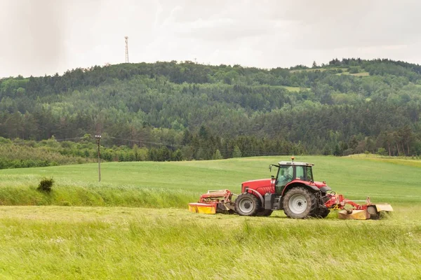 Bekerja di pertanian. Sebuah traktor merah memotong padang rumput. — Stok Foto