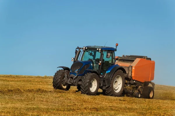 Traktor biru mengumpulkan jerami kering. Pekerjaan pertanian di pertanian di Republik Ceko . — Stok Foto