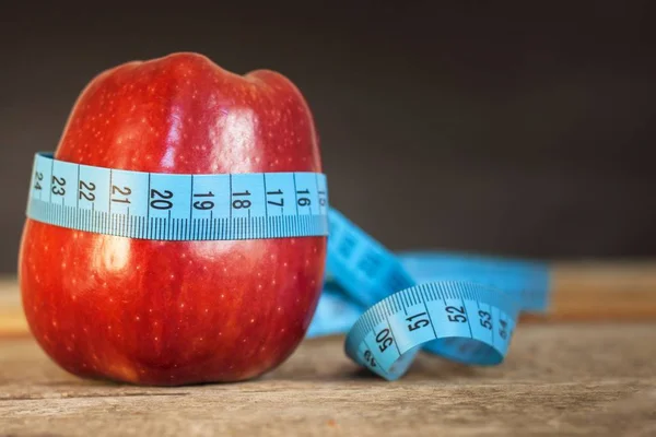 Manzana roja con cinta métrica para medir la longitud sobre un fondo de madera, dieta, estilo de vida saludable . — Foto de Stock