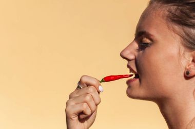 Young beautiful girl eats chilli. Portrait of a beautiful woman with a hot pepper. Healthy diet. Spicy food. clipart