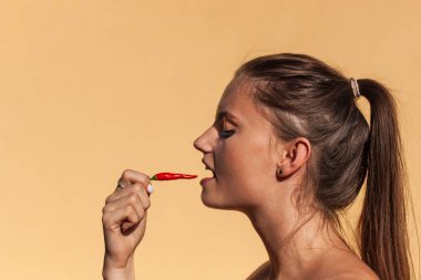 Genç güzel kız biber yiyor. Acı biber ile güzel bir kadın portresi. Sağlıklı beslenme. Baharatlı gıda.