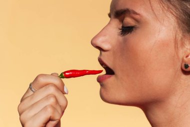 Young beautiful girl eats chilli. Portrait of a beautiful woman with a hot pepper. Healthy diet. Spicy food. clipart