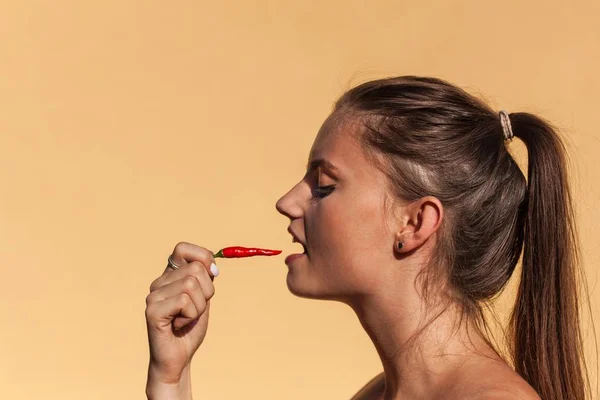 Jovem menina bonita come pimenta. Retrato de uma mulher bonita com uma pimenta. Dieta saudável. Comida picante . — Fotografia de Stock