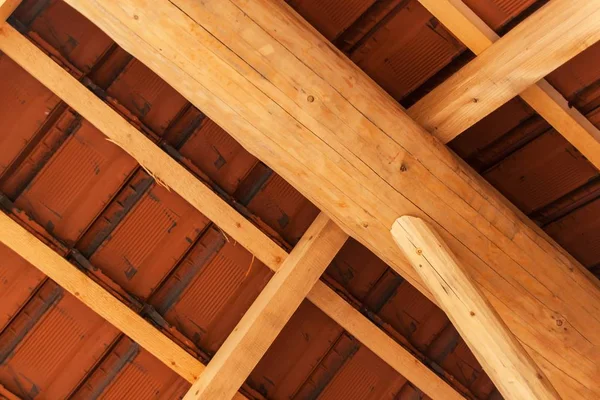Houten balken onder een dak van rode baksteen tijdens. Detail van houten dakstructuur. — Stockfoto