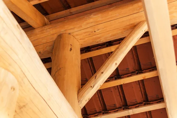 Vigas de madeira sob um telhado de tijolo vermelho durante. Detalhe da estrutura do telhado de madeira . — Fotografia de Stock