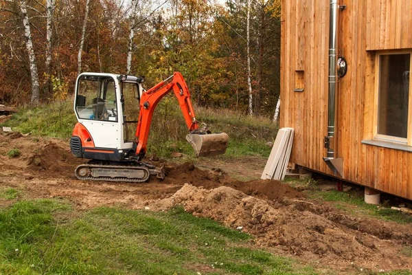 Minibagger auf Baustelle. Bau eines Einfamilienhauses in der Nähe eines Waldes. — Stockfoto