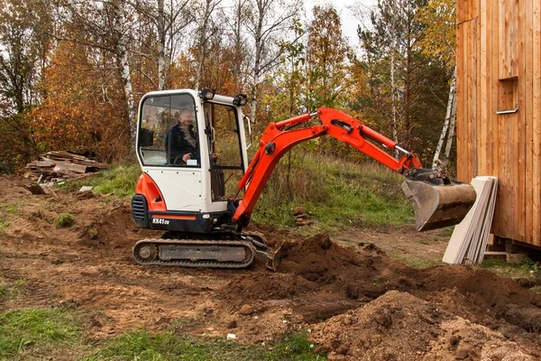 Mini escavadeira no canteiro de obras. Escavadeira regula o terreno em torno da casa . — Fotografia de Stock