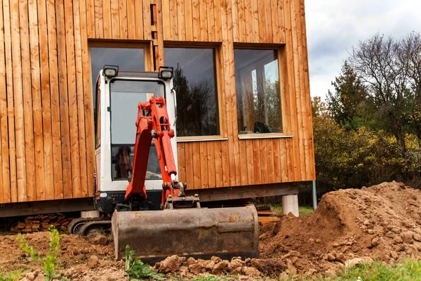 Lavori sul cantiere di una casa ecologica. L'escavatore regola il terreno. Un piccolo scavatore nel giardino . — Foto Stock