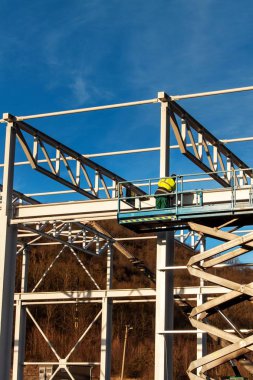 Çelik yapısı henüz tamamlanmamıştır. Metal salonları montajı. Yükseklikte çalışıyorum. Bir inşaat sahasında güneşli bir gün.