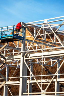 Çelik yapısı henüz tamamlanmamıştır. Metal salonları montajı. Yükseklikte çalışıyorum. Bir inşaat sahasında güneşli bir gün.