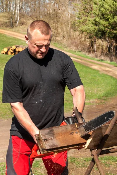 Hombre cortando con motosierra eléctrica. Trabajo en la granja. Preparación de madera para calefacción. El leñador trabaja con la sierra . — Foto de Stock
