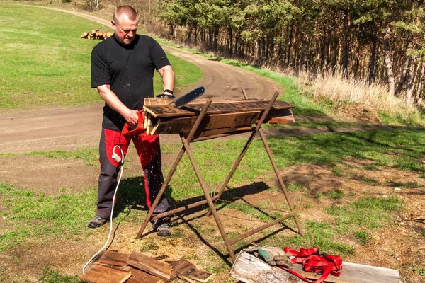 Man cutting with electric chain saw. Work on the farm. Wood preparation for heating. The woodcutter works with the saw.