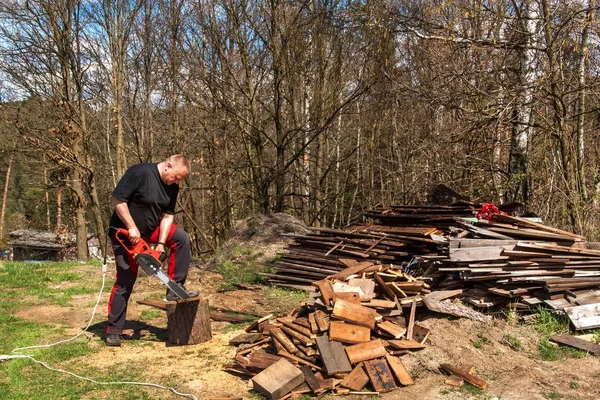 Man cutting with electric chain saw. Work on the farm. Wood preparation for heating. The woodcutter works with the saw.