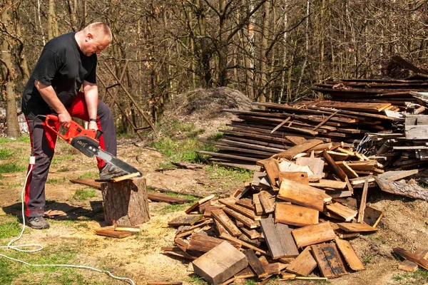 Hombre cortando con motosierra eléctrica. Trabajo en la granja. Preparación de madera para calefacción. El leñador trabaja con la sierra . — Foto de Stock