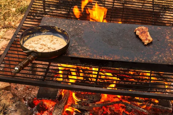 Panela esmaltada a arder. Preparação de molho de bife de cogumelos. Fogo no acampamento . — Fotografia de Stock