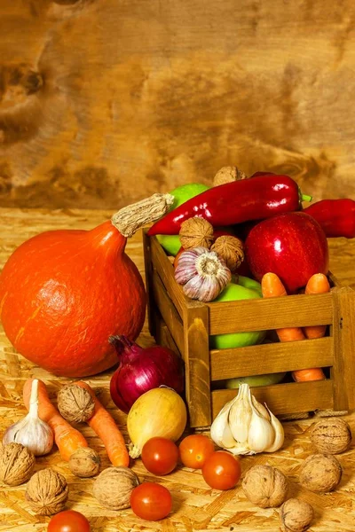 Mele e verdure in una scatola di legno sul tavolo. Raccolta autunnale di frutta e verdura. Mele, peperoni, aglio, noci e pomodori su tavola di legno. Cibo sano . — Foto Stock