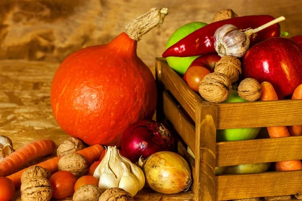 Mele e verdure in una scatola di legno sul tavolo. Raccolta autunnale di frutta e verdura. Mele, peperoni, aglio, noci e pomodori su tavola di legno. Cibo sano . — Foto Stock