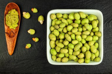 Wasabi kaplı fıstıklar tahtada. Japon Wasabi Baharatı. Siyah bir tabakta siyah fındıklı yeşil wasabi fıstığı.