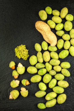 Wasabi kaplı fıstıklar tahtada. Japon Wasabi Baharatı. Siyah bir tabakta siyah fındıklı yeşil wasabi fıstığı.