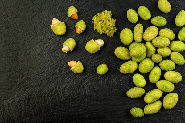 Wasabi Coated Peanuts on slate board. Japanese Wasabi Spice. Green wasabi peanuts on a black plate on a dark background. — Stockfoto